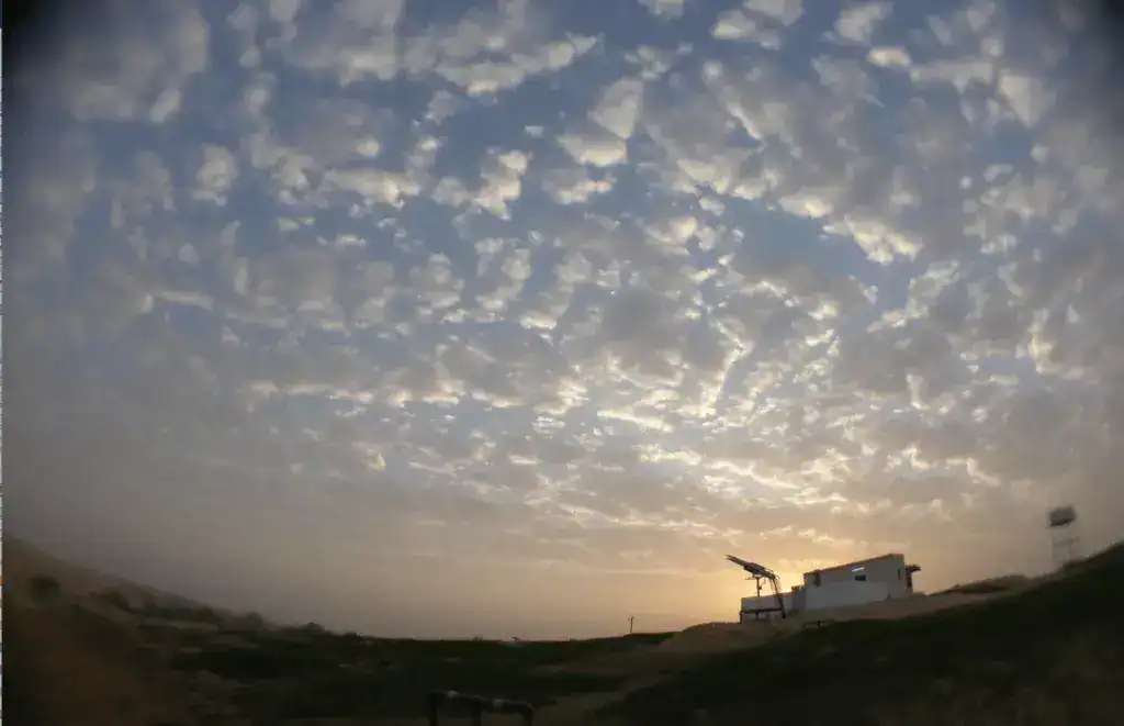 Wolkiger Himmel über einer Wüstenlandschaft mit Beobachtungsturm.