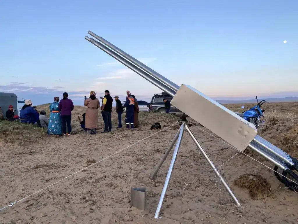 Alt-Text: Solarkocher in der Wüste mit Menschen, die ihn beobachten und fotografieren.
