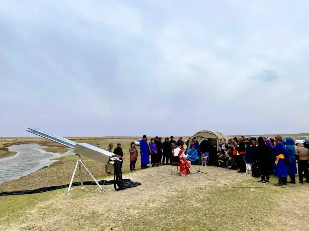 Menschen versammeln sich bei einer Wüstenbegrünungsveranstaltung mit Solartechnik im Hintergrund.